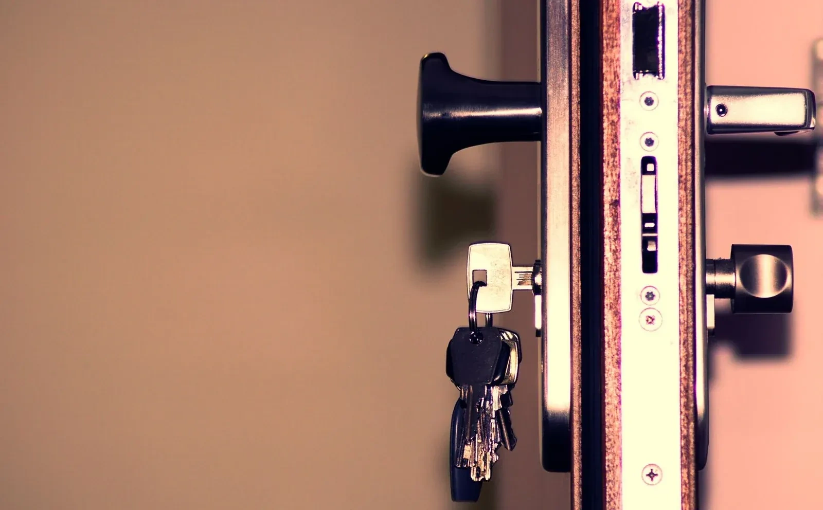 Bunch of keys hanging from a key in a door lock, beside a black knob and the door's metal edge plate.